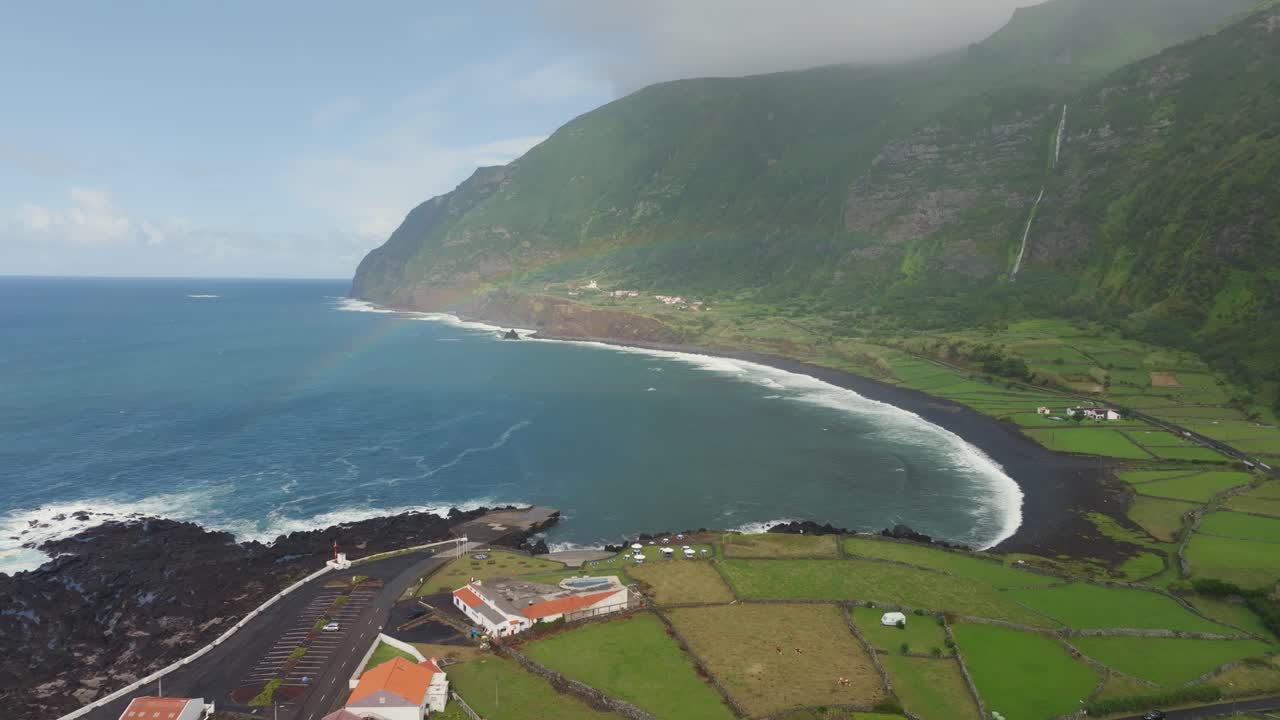 Vista aerea del villaggio di Faja Grande sull'isola di Flores con un arcobaleno vibrante che si inarca sopra le case e le onde dell'Atlantico settentrionale