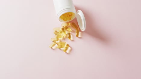 video of white pill box spilling oil capsules on pink background with copy space