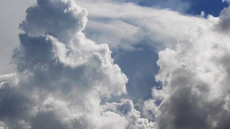 Blauer Sommerhimmel mit dichten, schweren Regenwolken, die über den Himmel ziehen.