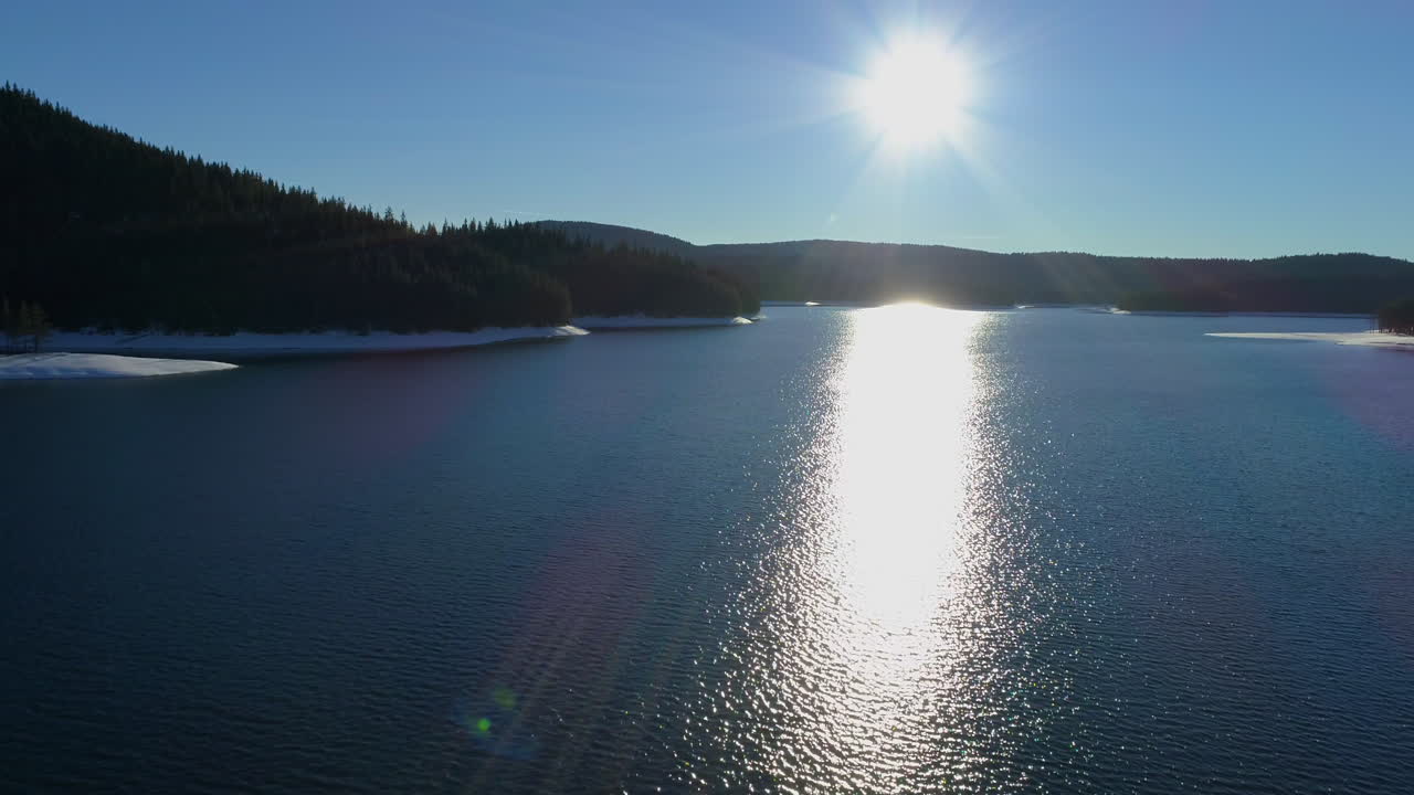 Flying over a mountain lake in winter. The sun shines brightly and is reflected in the water