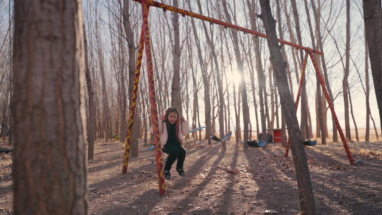 Young girl swinging beneath tall trees in a peaceful forest playground setting.