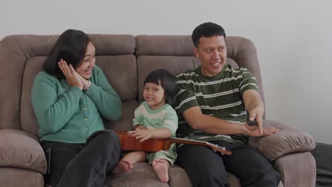 Happy-Asian-Family-Watching-TV-Together-And-Having-Fun-Lying-On-Sofa-In-Living-Room-At-Home