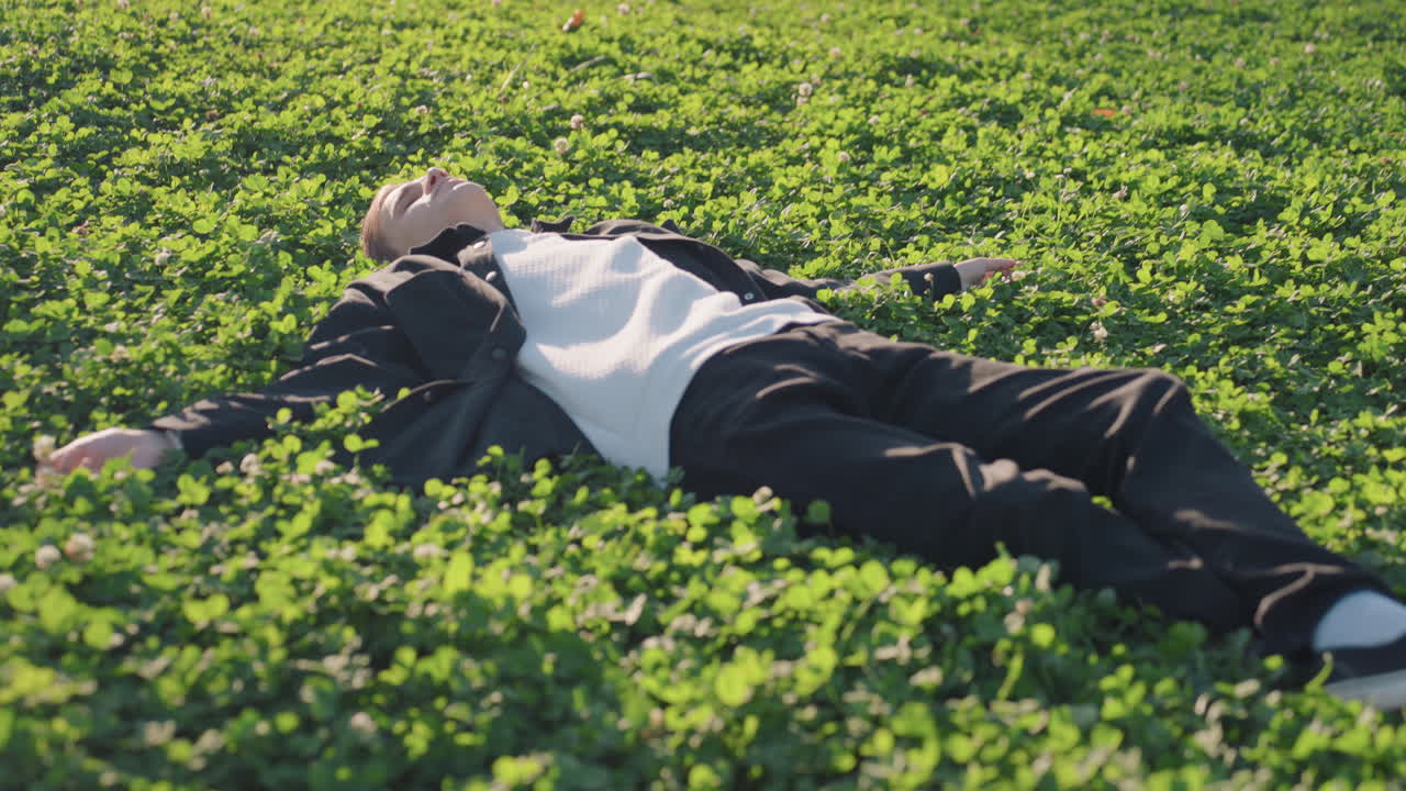 Man resting peacefully. Closeup of man reclining on grass. Serene portrait of man basking in sunlight outdoors. Tranquil scene capturing man relaxing amidst vibrant meadow greenery with soft smile