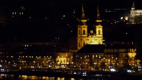 Budapest-city-center-view-with-illuminated-church-tower-and-Danube-river-at-night,-gothic-architecture,-light-reflections,-distant-shot