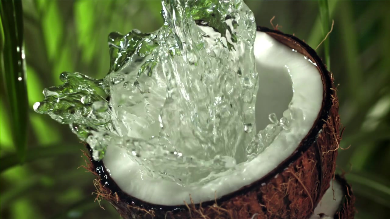 Fresh Water Pouring into a Halved Coconut with Splashes