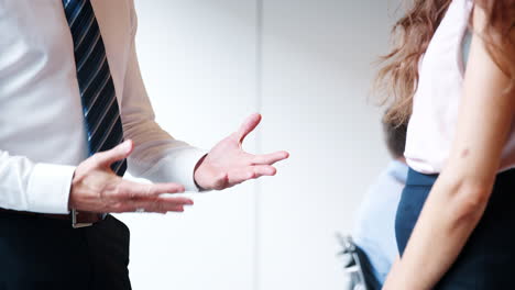 Close-Up-Of-Businessman-And-Businesswoman-Shaking-Hands-In-Modern-Boardroom-With-Colleagues-Meeting-Around-Table-In-Background-Shot-In-Slow-Motion