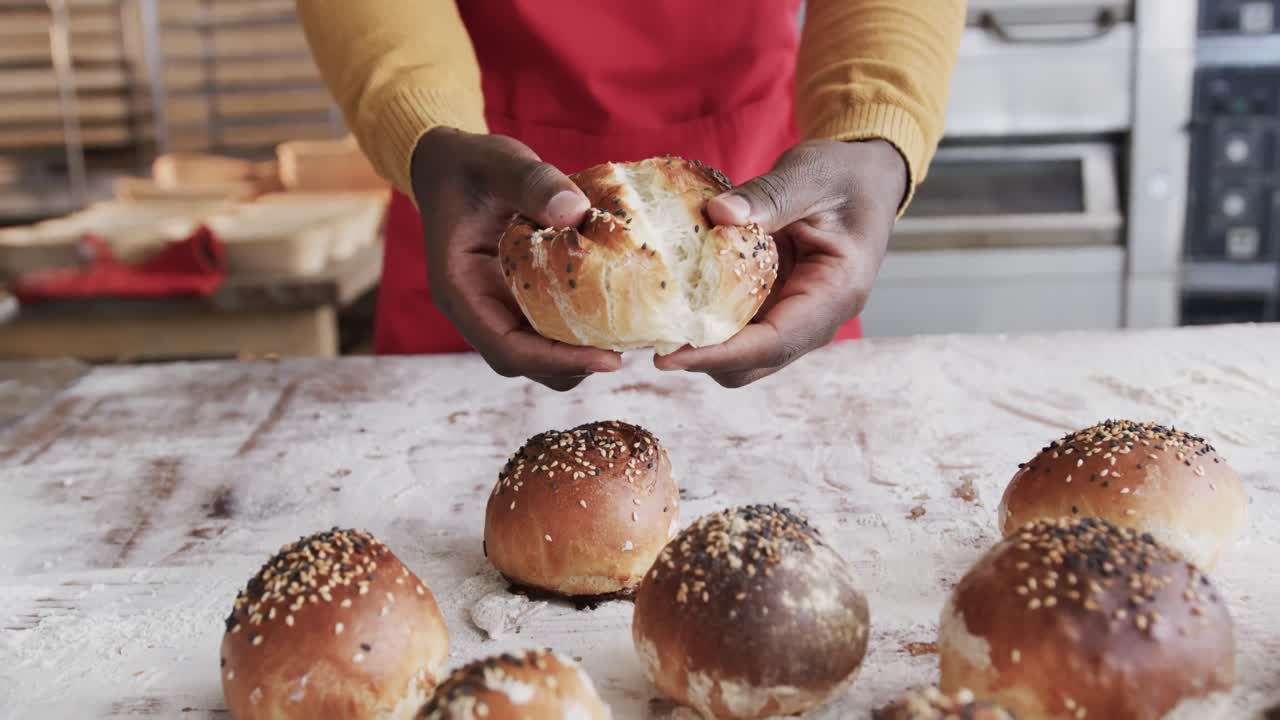 Midsection of african american male baker working in bakery kitchen, ripping roll, slow motion