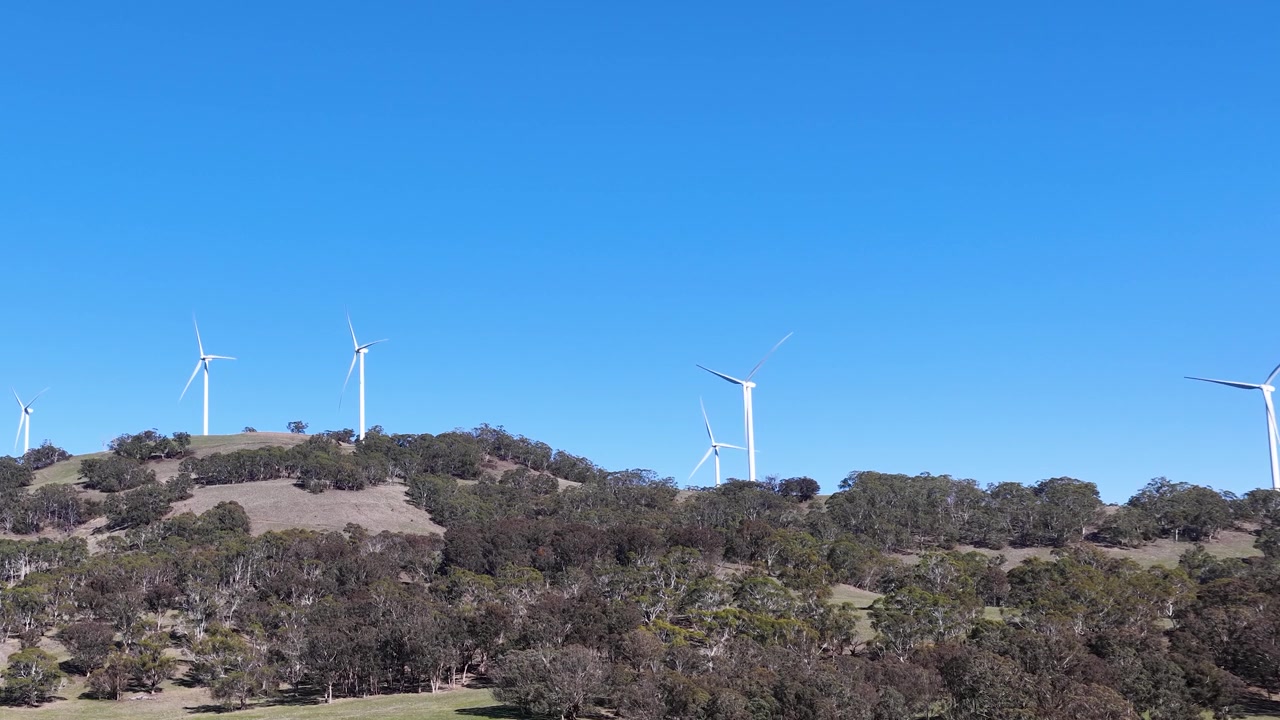 Inquadratura ampia di turbine eoliche bianche in rotazione su una cresta boscosa nel Nuovo Galles del Sud