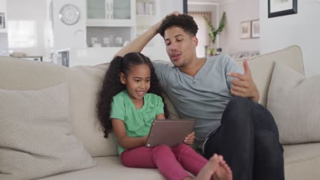 Glücklicher-Gemischtrassiger-Vater-Und-Tochter,-Die-Auf-Dem-Sofa-Sitzen-Und-Ein-Tablet-Benutzen