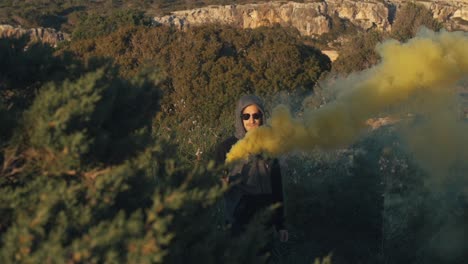 slow motion footage of a mysterious man holding a yellow smoke bomb in his hand - outside in a tropical scenery.