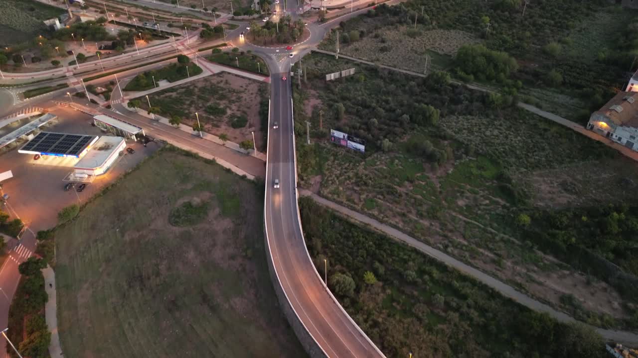 Aerial view of an urban roundabout enveloped by lush vegetation and lit-up roads at dusk, highlighting the balance of nature and infrastructure within the cityscape
