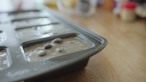un mini molde para pan lleno de masa de pan de calabacín y arándanos se retira para hornear