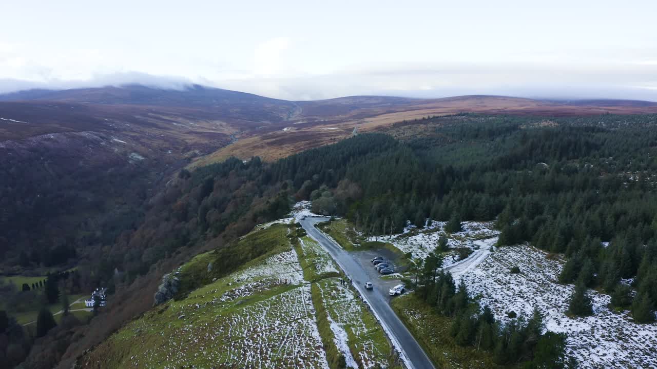 vista aérea de un automóvil conduciendo a través de un bosque cubierto de nieve en las montañas wicklow, con personas disfrutando del telón de fondo del bosque nevado