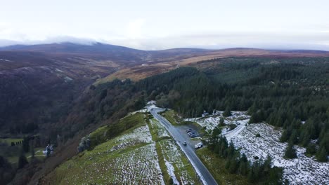 Vista-Aérea-De-Un-Automóvil-Conduciendo-A-Través-De-Un-Bosque-Cubierto-De-Nieve-En-Las-Montañas-De-Wicklow,-Con-Gente-Disfrutando-Del-Fondo-Del-Bosque-Nevado