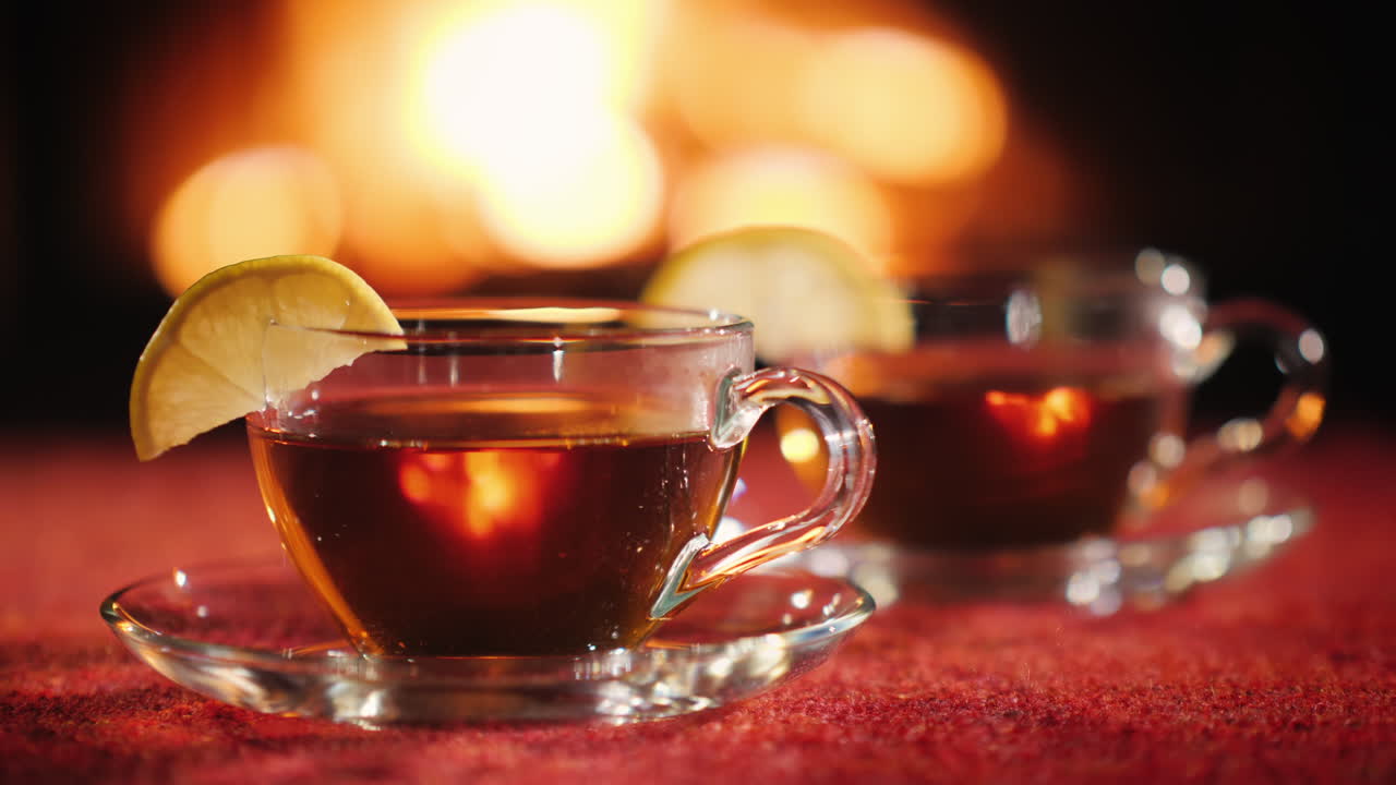 две чашки с чаем и лимоном на фоне камина, в котором горит огонь