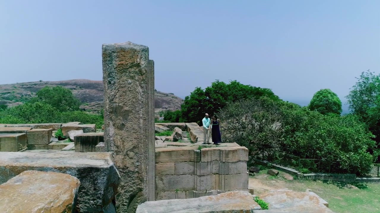 Una coppia si trova insieme tra antiche rovine in pietra con una vegetazione lussureggiante e colline sullo sfondo