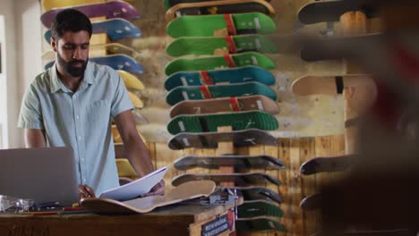 video of happy middle eastern male skateboarder using laptop in skate shop