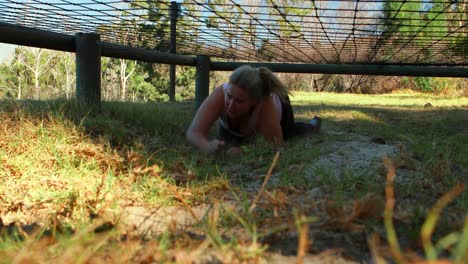 determined woman crawling under the net during obstacle course