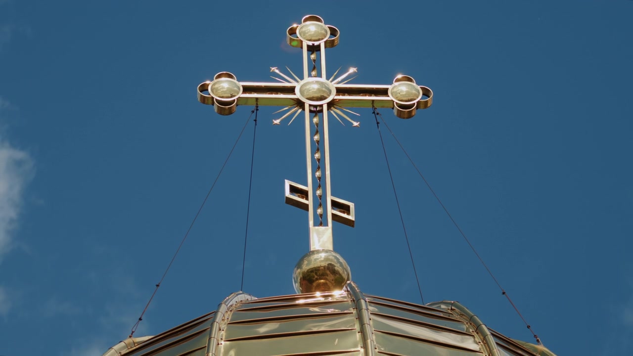 Low angle view of a golden Orthodox church cross illuminated by sunlight against a clear blue sky