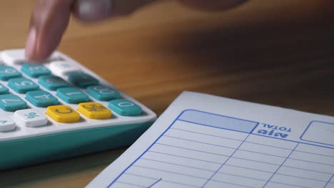 Close-Shot-of-a-Man-Writing-Out-a-Bill-with-a-Calculator