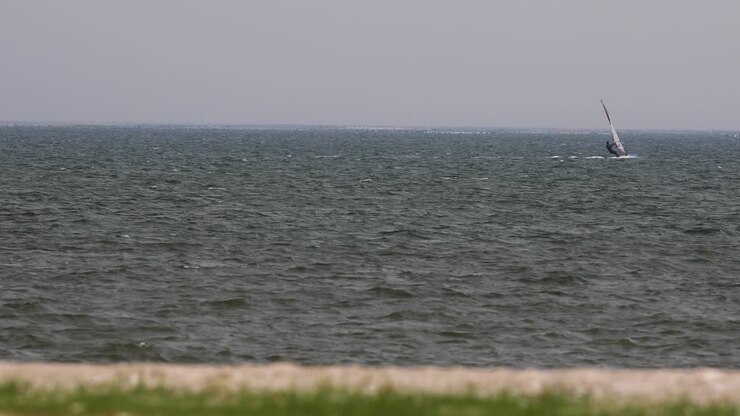 Vindsurfer sejler over de blæsende have med et overskyet gråt skydække. Zoomoptagelse i 4K