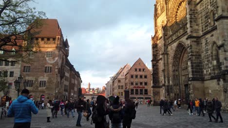 slow pan and tilt of the historic chruch lorenzkirche in nuremberg. the two high towers are shining golden in the last sunlight of the day at sunset while many people are busy walking in the pedestrian zone below.