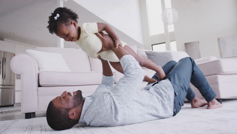 father playing with baby daughter lifting her in the air at home