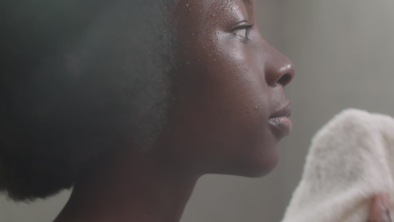 Black Woman Wiping Face with Towel in Bathroom