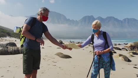 senior hiker couple wearing face masks with backpacks and hiking poles reading maps while hiking