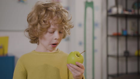 little boy eating an apple in classroom in a montessori school