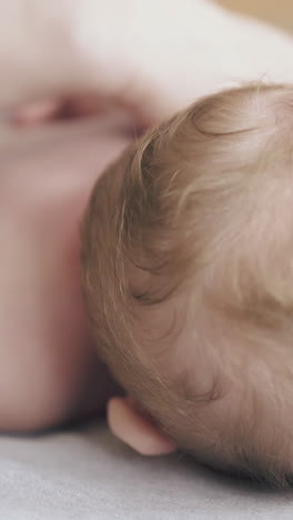 infant boy with short blond hair lies on stomach on changing table and professional nurse massages back close view