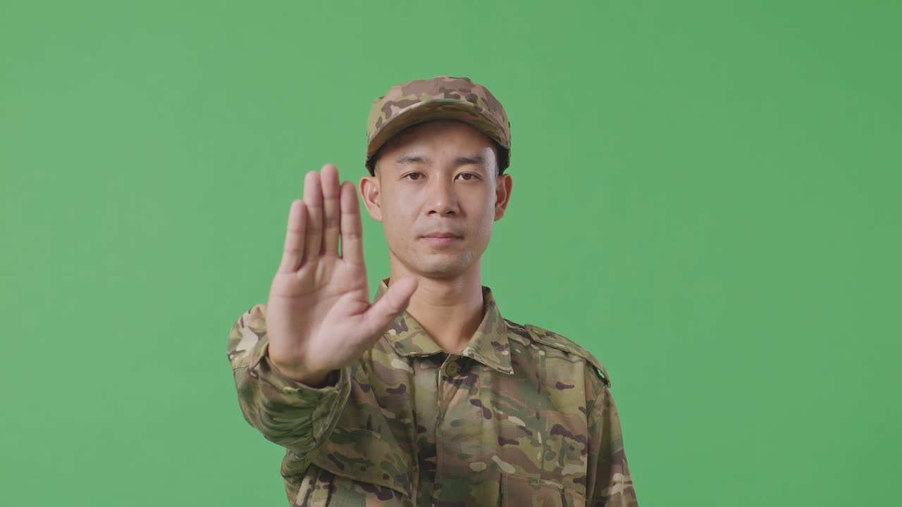 Close Up Of Asian Man Soldier Looking At Camera And Disapproving With No Hand Sign While Standing In The Green Screen Background Studio