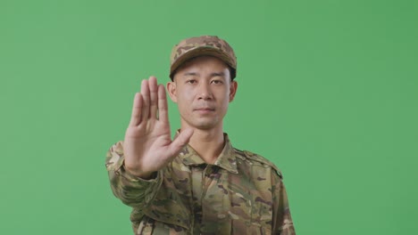 Close Up Of Asian Man Soldier Looking At Camera And Disapproving With No Hand Sign While Standing In The Green Screen Background Studio