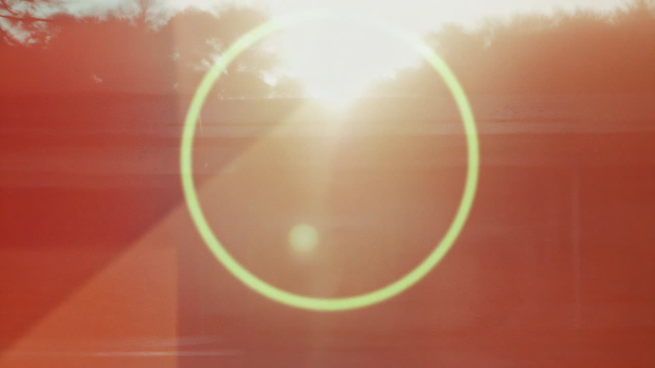 Rising sun peeking above roofline and initiating pale green lens flare across treetops