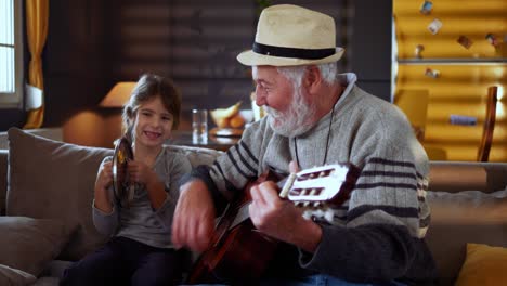 portrait of a cheerful old man with a hat playing guitar and looking at the camera while his granddaughter plays next to him