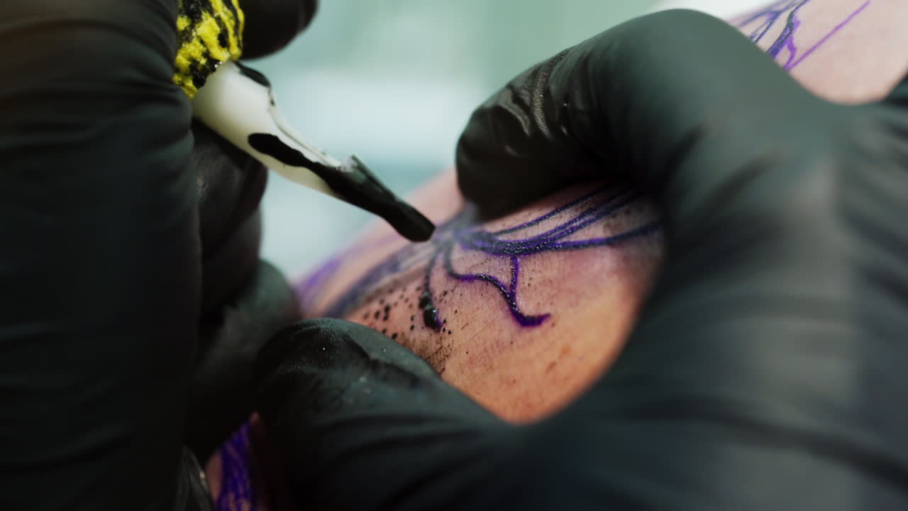 Covering the sketched picture with black ink. Tattooist wearing black gloves uses special ink machine at work. Close up.