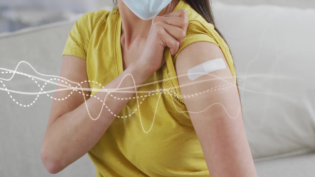 Mid adult woman pulling back sleeve on sofa showing medical bandage with waveform graphics flowing