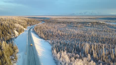 rv in snowy alaska, aerial, pan, drone shot, following camper on slippery road, in middle of frosty forest, at sunset, in northern usa