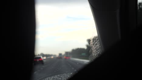 Car-drives-through-rain-with-droplets-sliding-along-windshield-in-slow-motion