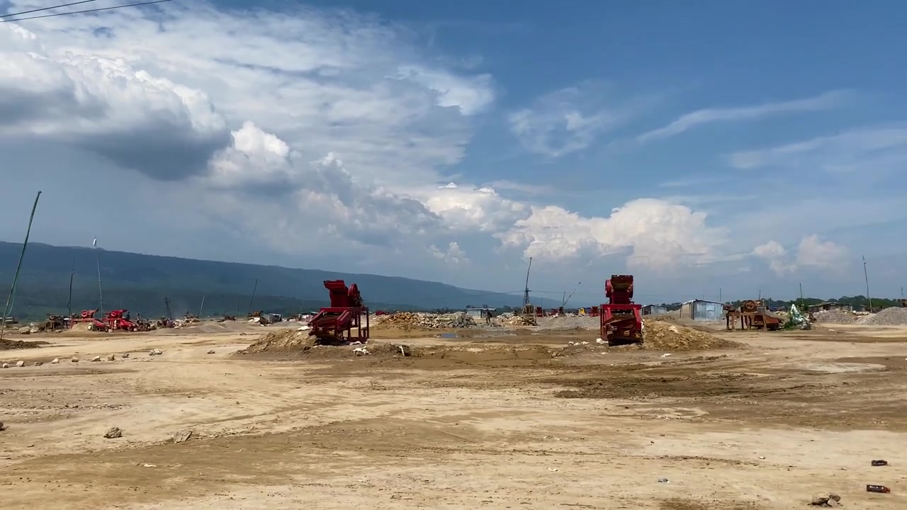 Cantiere di frantumazione pietre con macchinari, cumuli di pietre, lungo le colline sotto un cielo nuvoloso a Bholaganj, Sylhet, Bangladesh.
