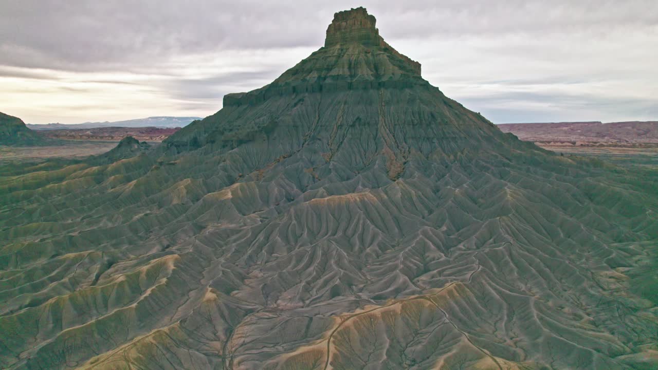 Aerial 4K drone reveal of Utah’s Factory Butte badlands, with deeply eroded gullies, sharp ridgelines, dramatic desert topography with intricate textures and earthy tones, rugged, otherworldly terrain