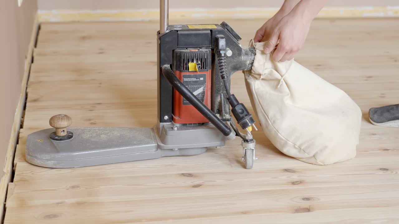 Hands place bag and tighten to close dust collection for electric edge sander working along wood plank flooring edge
