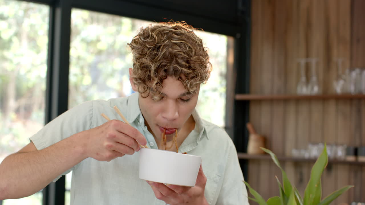 Young man enjoying noodles with chopsticks at home, savoring every bite