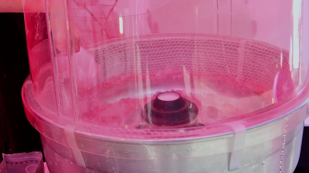 Candy floss being made with a machine at a street fair in England.  Slow motion, zoom out.