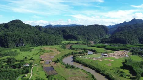 upward drone shot showing extensive green farmlands, mountains and a winding river under blue sky