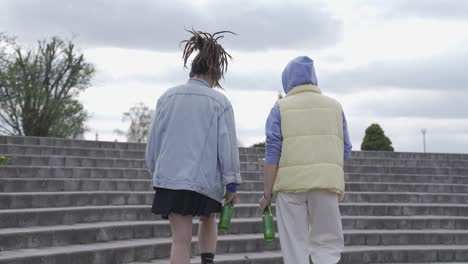 two urban girls sitting on stairs with beer bottles and pizza box