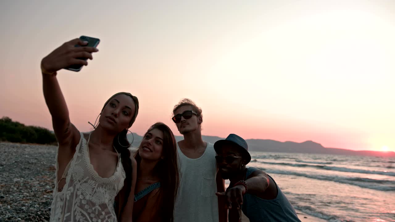 jóvenes amigos hipsters multiétnicos tomando selfies en la playa al atardecer