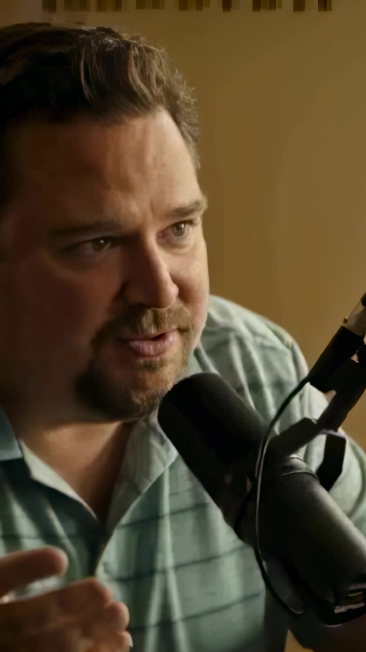 Vertical video: Answering offscreen question, podcast host leaning, speaking into mic, striped polo