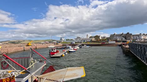 camera pans from a bright orange lifebuoy to a harbor with moored sailing boats under a cloudy sky, capturing a breezy seaside atmosphere