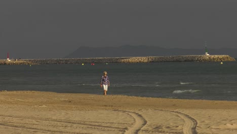 Mujer-Soltera-Jubilada-De-Vacaciones-Dando-Un-Relajante-Paseo-Por-La-Playa-Al-Amanecer